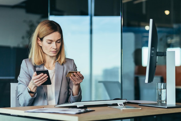 Seriöser Geschäftsfrau-Banker führt Bankgeschäfte mit einer Kreditkarte durch und eine Anwendung am Telefon arbeitet in einem modernen Bankbüro