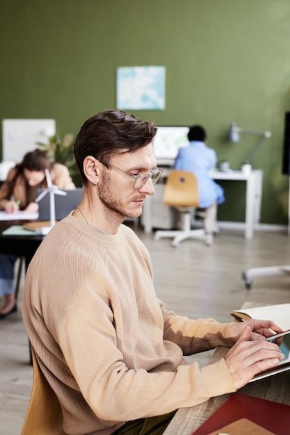 Seriöser Geschäftsmann mit Brille, der sich am Tisch auf seine Online-Arbeit auf einem digitalen Tablet konzentriert