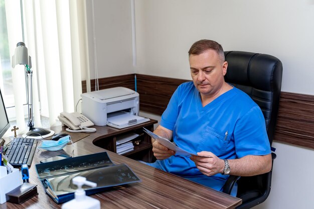 Seriuos médico masculino leyendo diagnóstico médico. Sentado en el gabinete. Fondo de oficina interior moderno.