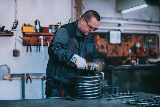 Serralheiro em roupas especiais e óculos de proteção trabalha na produção Processamento de metal com rebarbadora Faíscas em metalurgia