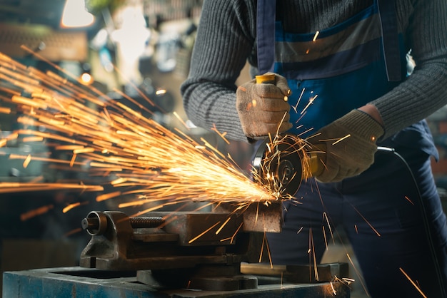 Serralheiro em roupas especiais e óculos trabalha na produção. processamento de metal com rebarbadora