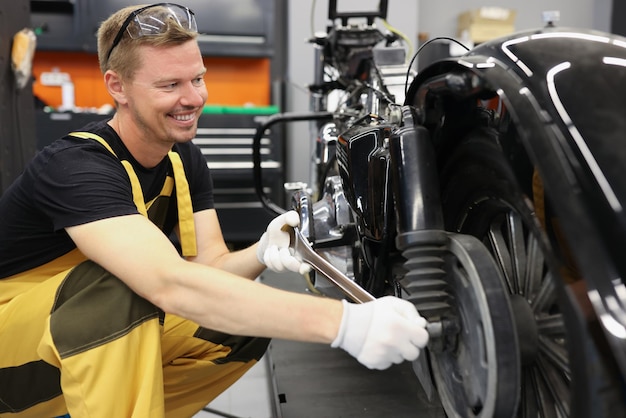 Serralheiro sorridente com chave inglesa perto da roda de motocicleta em oficina de automóveis motocicleta serviço de garantia