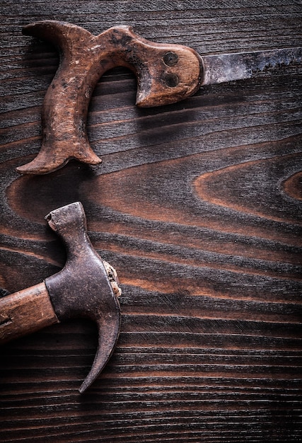 Serrucho antiguo oxidado con martillo de orejas en el concepto de construcción de fondo de madera oscura vintage