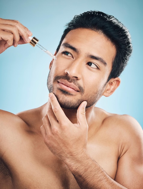 Foto serum de beleza e anti-envelhecimento facial com um homem em estúdio em um fundo azul para cuidados com a pele ou cuidado com a pele óleo de luxo ou bem-estar com um homem bonito no banheiro para aplicar um produto à sua pele