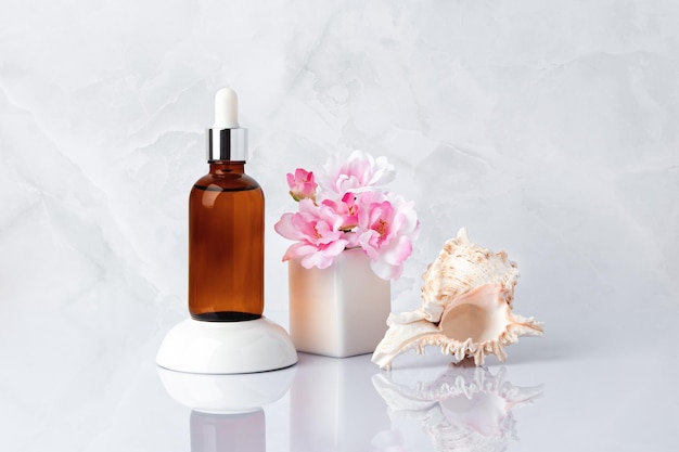 Foto serum facial concha de mar botella de vidrio marrón vial ramo de flores rosadas de primavera aceite de masaje aromático y flor de cerezo concepto de hidratación de la piel cosmético de spa orgánico natural producto de cuidado de belleza