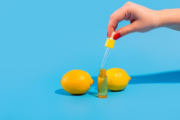 Serum in einer transparenten Flasche mit einer Pipettenhand mit gelben Zitronen auf blauem Hintergrund