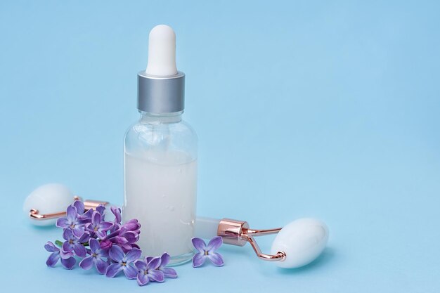 Serum mit Blumenextrakten für die Hautpflege Gesichtsmassagerolle auf blauem Hintergrund