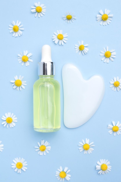 Serum mit Blumenextrakten für die Hautpflege Gua sha Stein für die Gesichtsmassage Kamillenblüten auf gelbem Hintergrund Spa-Konzept für Gesichts- und Körperpflege