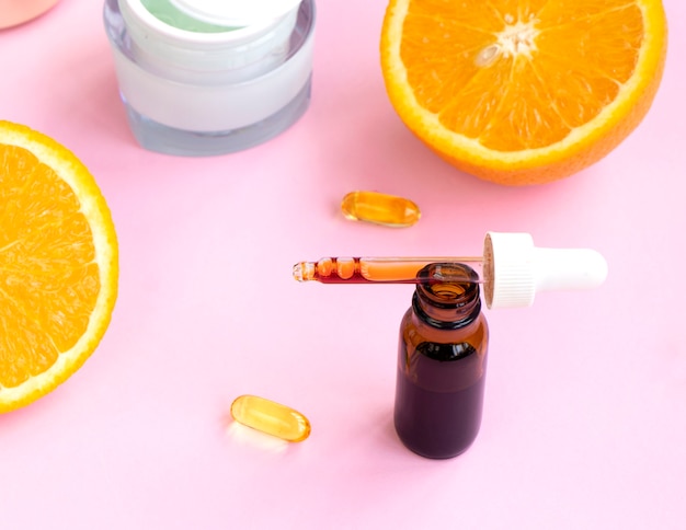 Serum mit Vitamin C mit ätherischem Öl eine Medizinflasche Orangen und Creme auf rosa Hintergrund