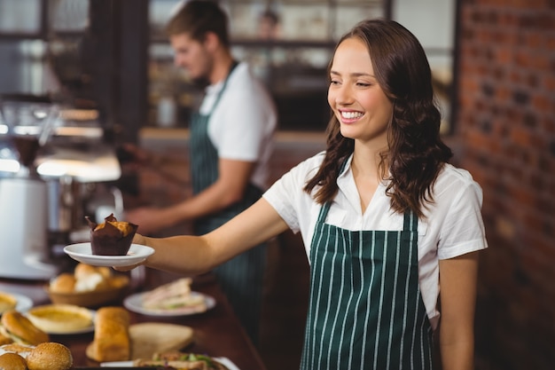 Servadeira sorridente servindo um muffin