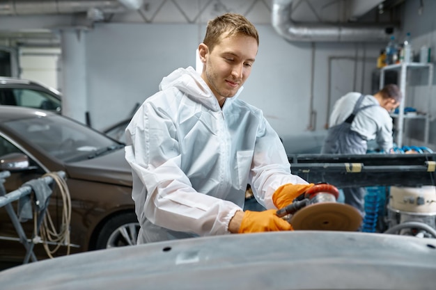 Foto servicemann poliert karosserieteile mit schleifmaschine in der werkstatt. garagenlackierung autoservice