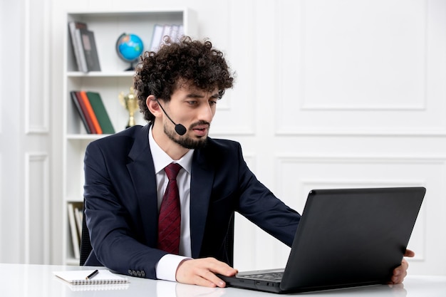 Servicio al cliente apuesto joven en traje de oficina con computadora portátil y auriculares tocando la computadora portátil