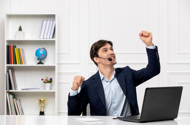 Servicio al cliente, el lindo chico moreno del traje con la computadora portátil emocionado levantando los puños