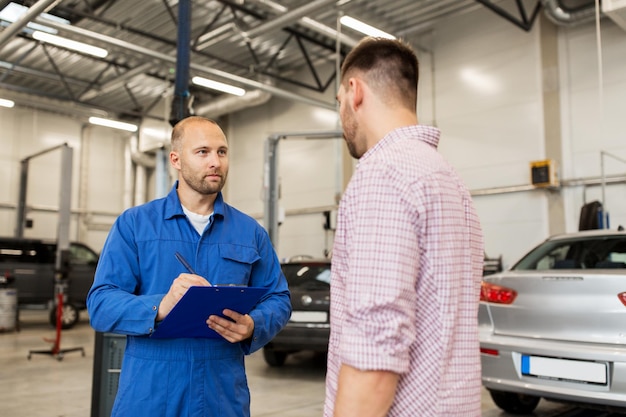 servicio automático, reparación, mantenimiento y concepto de personas: mecánico con portapapeles hablando con el hombre o el propietario en la tienda de autos