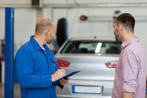 servicio automático, reparación, mantenimiento y concepto de personas: mecánico con portapapeles hablando con el hombre o el propietario en la tienda de autos
