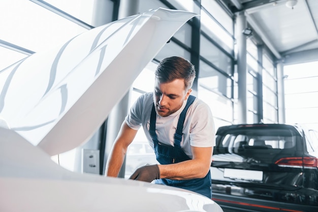 Servicio de calidad Joven con camisa blanca y uniforme azul repara automóvil