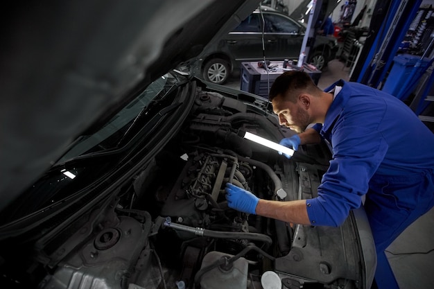 servicio de camión, reparación, mantenimiento y concepto de personas - mecánico de automóviles con lámpara trabajando en el taller