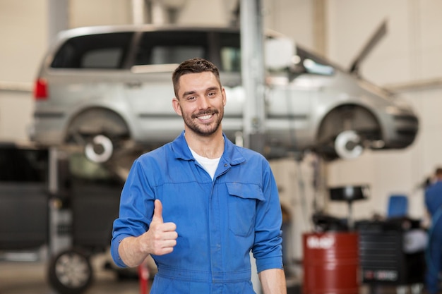 servicio de camión, reparación, mantenimiento, gesto y concepto de personas - feliz sonriente mecánico de automóviles o herrero mostrando los pulgares hacia arriba en el taller