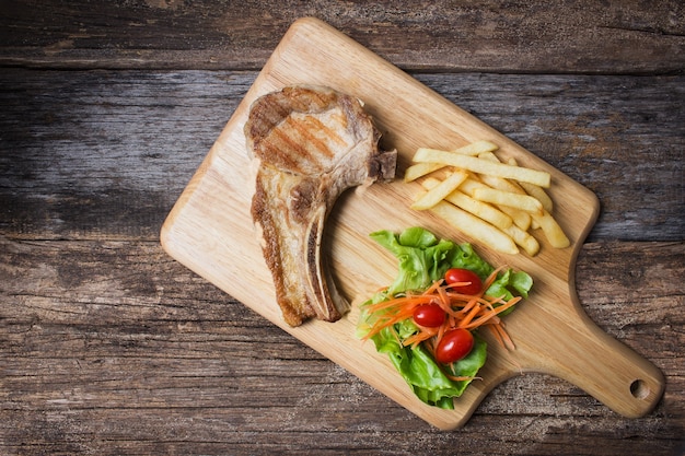 Servicio de chuleta de cerdo a la parrilla con vegetales en tablero de madera