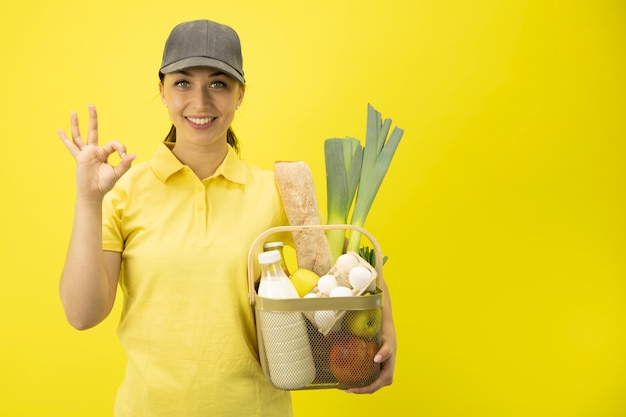 Servicio de entrega de alimentos chica con canasta de comestibles en la pared amarilla copia espacio