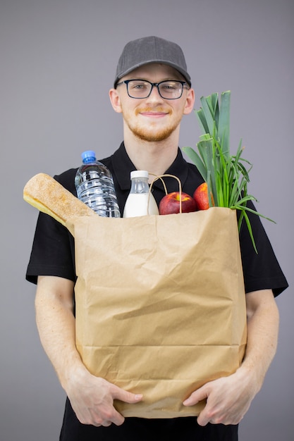 Servicio de entrega de alimentos hombre con caja de comestibles en pared gris aislado