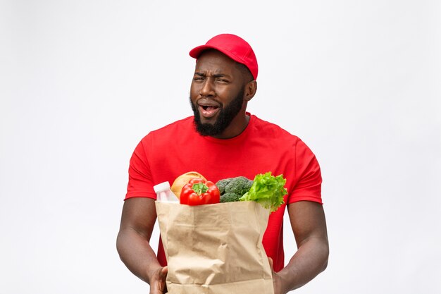 Servicio de entrega - Retrato de hombre de entrega serio afroamericano sosteniendo la bolsa de la compra