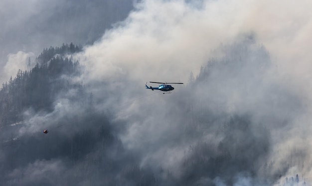 Servicio de incendios forestales Helicóptero sobrevolando BC Forest Fire y Smoke en la montaña cerca de Hope