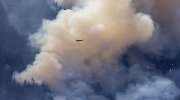 Servicio de incendios forestales Helicóptero sobrevolando BC Forest Fire y Smoke en la montaña cerca de Hope