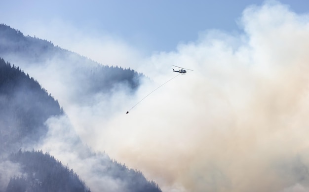 Servicio de incendios forestales Helicóptero sobrevolando BC Forest Fire y Smoke en la montaña cerca de Hope