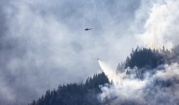 Servicio de incendios forestales Helicóptero sobrevolando BC Forest Fire y Smoke en la montaña cerca de Hope