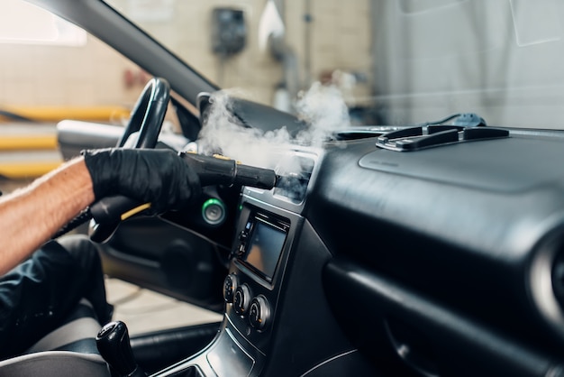 Foto servicio de lavado de autos, trabajador masculino con guantes quitando el polvo y la suciedad con un limpiador a vapor.