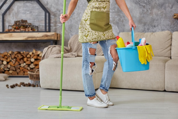 Servicio de limpieza. Cubo con esponjas, botellas de productos químicos y bastoncillo para trapear. Guantes de goma y toalla. Equipo para el hogar. Imagen recortada de una mujer con una fregona en la sala de estar