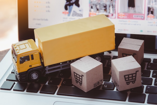 Servicio de logística y entrega: camiones y cajas de papel o paquetes con el logotipo de un carrito de compras en el teclado de una computadora portátil. Servicio de compra en la web online y ofrece entrega a domicilio.