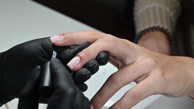 Servicio de manicura La manicurista pinta sus uñas con un esmalte de gel transparente Aplicando esmalte de uñas Uñas bien arregladas Un maestro de manicura pinta las uñas de un cliente en un salón de belleza