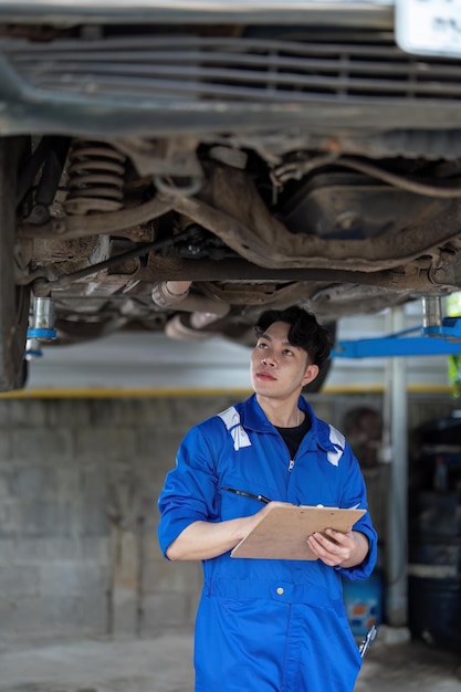 Servicio de mantenimiento del vehículo hombre asiático comprobando el estado del automóvil en el garaje Documento de lista de verificación de mantenimiento mecánico automotriz Concepto de servicio de reparación de automóviles