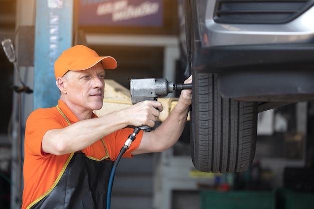 Servicio mecánico de neumáticos de coche con pistola de impacto en el garaje de la estación de servicio de reparación