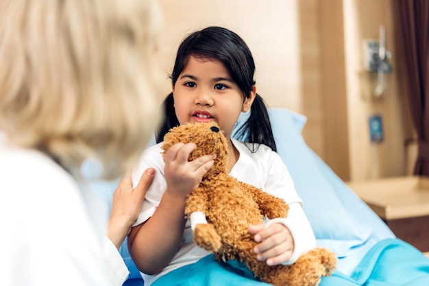 El servicio médico de la mujer sonriente mayor ayuda a discutir y consultar hablar con una paciente pequeña que le da un oso de peluche y verifica la información en el hospital