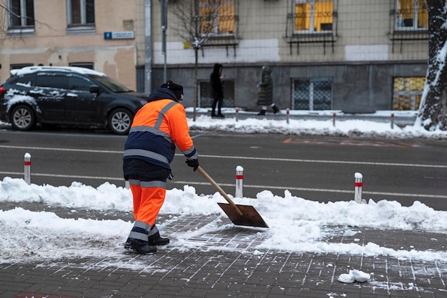 El servicio municipal de la ciudad limpia el sendero de la nieve después de la ventisca Trabajador paleando la nieve en la acera