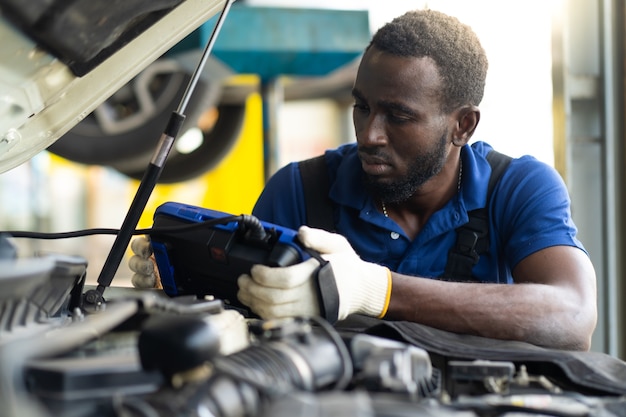 Foto servicio de reparación de mecánico de automóviles profesional y comprobación del motor del automóvil por computadora de software de diagnóstico. mecánico experto que trabaja en el taller de reparación de automóviles.