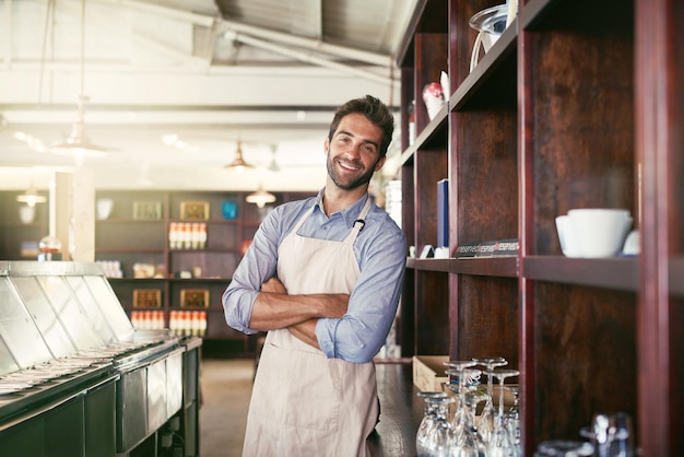 Foto servicio con una sonrisa retrato recortado de un joven barista de pie en una cafetería