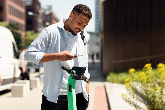 Servicios compartidos de scooters eléctricos joven negro que alquila scooters en la ciudad pagando en línea