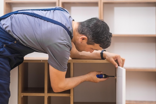 Servicios de fijación de muebles trabajador profesional en uniforme atornillando clavos en panel de madera