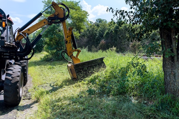 Los servicios viales se dedican a un tractor con una cortadora mecánica que corta el césped en el lado de la carretera asfaltada