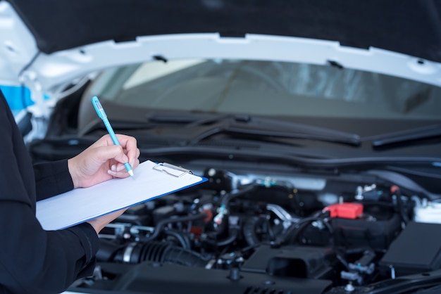 Serviço de carro, reparo, conceito de manutenção - homem mecânico asiático ou smith escrevendo para a área de transferência na oficina ou armazém, técnico, fazendo a lista de verificação para a máquina de reparo para um carro novo