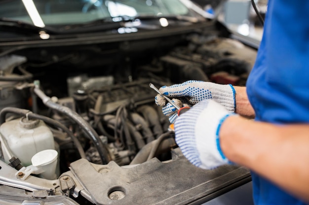 serviço de carro, reparo, manutenção e conceito de pessoas - homem mecânico com chave inglesa e lâmpada trabalhando na oficina