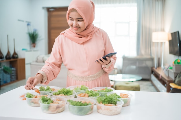 Serviço de catering caseiro para mulheres asiáticas muçulmanas a preparar lancheira para encomenda online de comida take-away