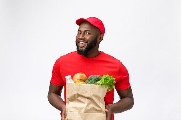 Serviço de entrega - homem afro-americano bonito entregador carregando pacote de comida e bebida da loja.