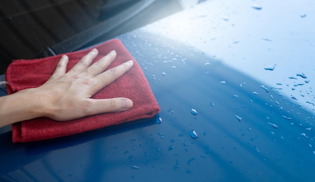 Serviço de lavagem de carros Mão de homem segurando carro azul de polimento de pano de microfibra vermelho e gota d'água após a limpeza