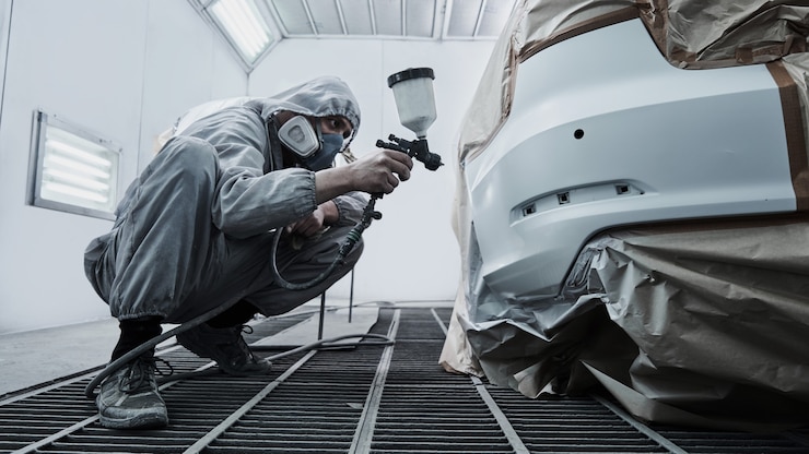 Foto serviço de pintura e reparação de automóveis. mecânico de automóveis de macacão branco pinta o carro com pulverizador aerógrafo na câmara de pintura
