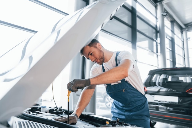 Serviço de qualidade jovem de camisa branca e uniforme azul repara automóvel